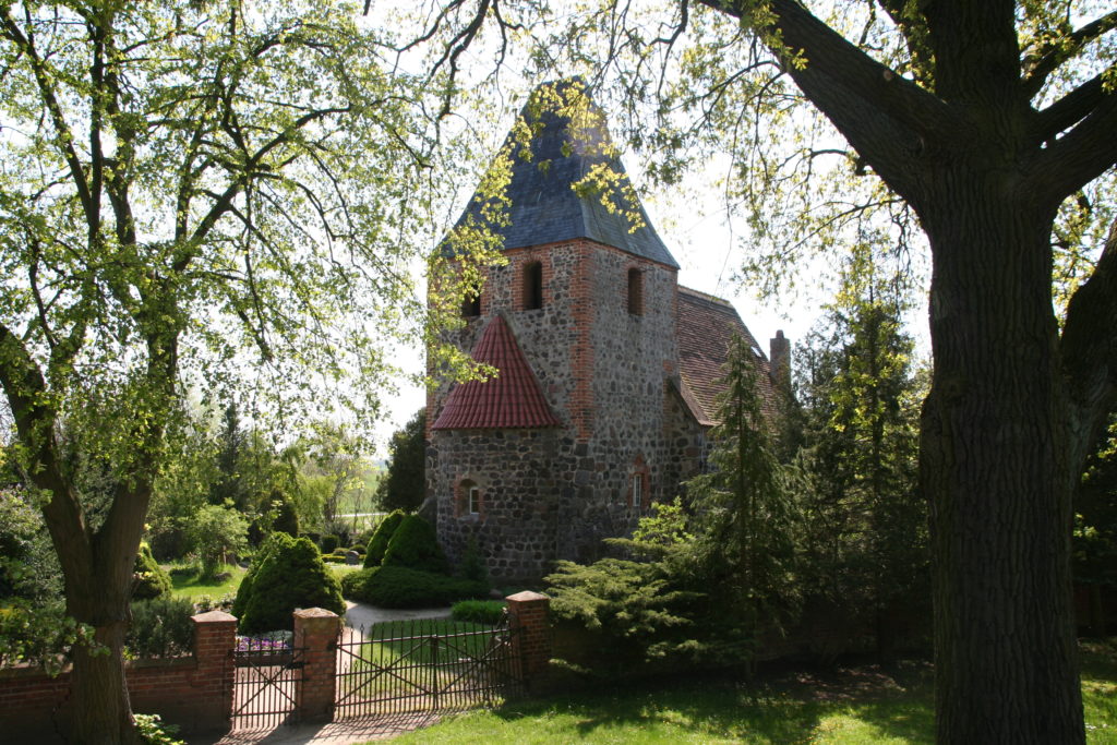 Kirche in Beelitz mit Bäumen und Sträuchern.