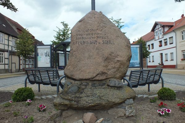 Gedenkstein mit Inschrift. Dahinter zwei Sitzbänke